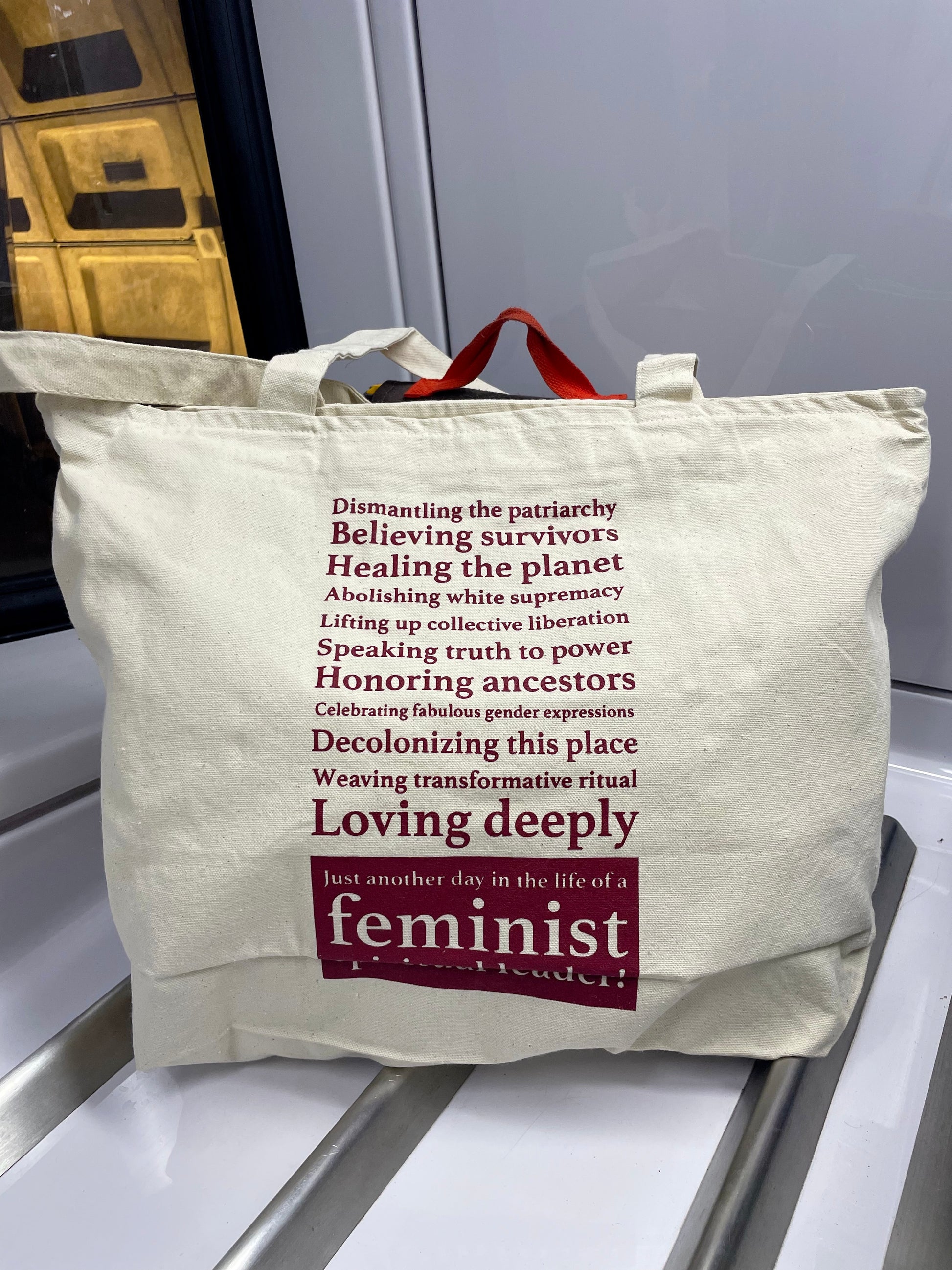 cream color tote bag with feminist text on a metallic surface